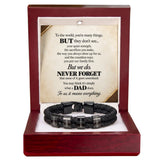 A black braided cord bracelet with silver engraved metal beads and a black clasp, presented inside an open reddish-brown wooden gift box. The box contains a printed message card dedicated to a father.