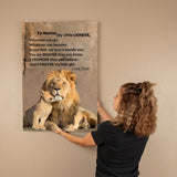 Woman hanging a framed picture of a lion and cub with a motivational quote on a beige wall.