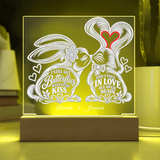 Personalized acrylic LED light box featuring two kissing rabbits with hearts and custom text, displayed on a wooden base with warm yellow lighting.