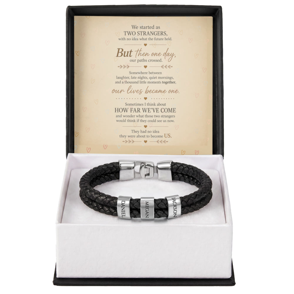 A black braided leather bracelet with silver metal accents engraved with 'LOVE' and 'FOREVER', presented in an open white gift box with a black outer lid. The inside lid features a printed sentimental message card.