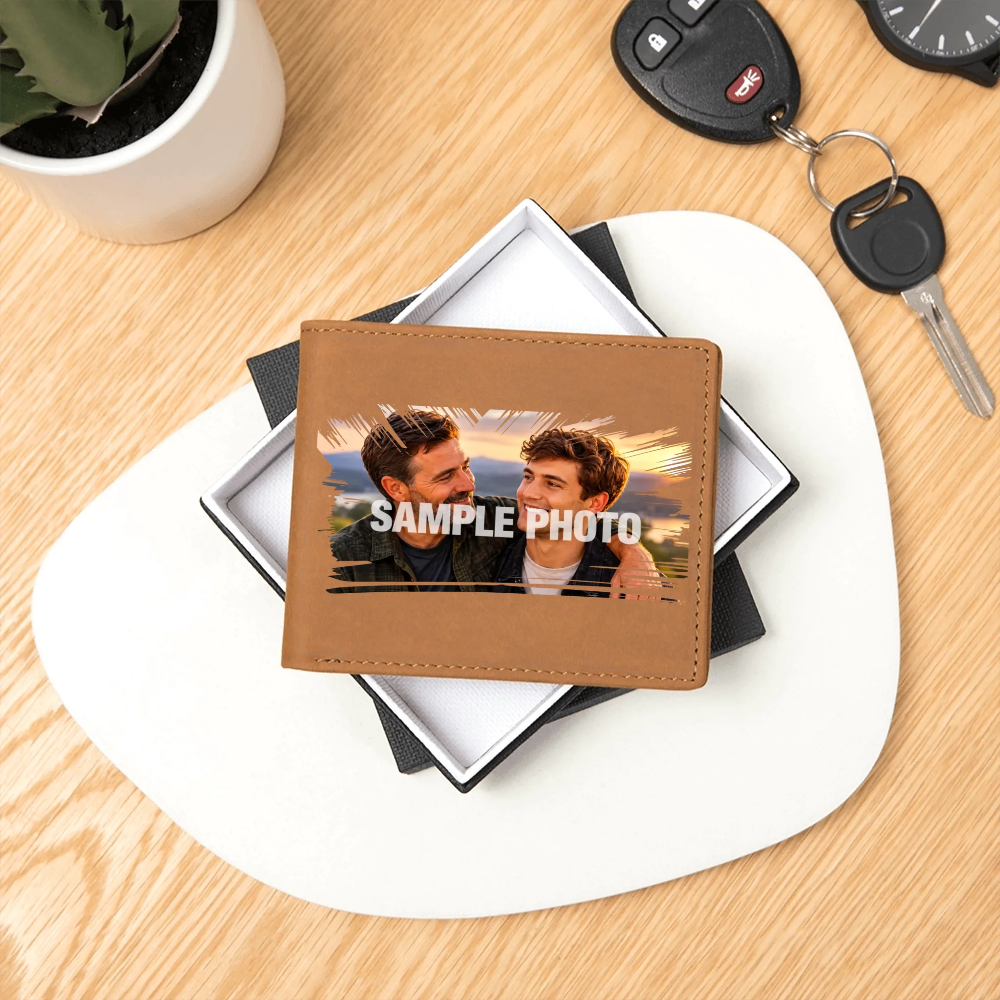 A personalized brown faux-leather bifold wallet with a custom photo of two men and the text 'SAMPLE PHOTO' printed across the front, displayed on a white and black gift box on a light wood desk.