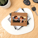 A personalized brown faux-leather bifold wallet with a custom photo of two men and the text 'SAMPLE PHOTO' printed across the front, displayed on a white and black gift box on a light wood desk.