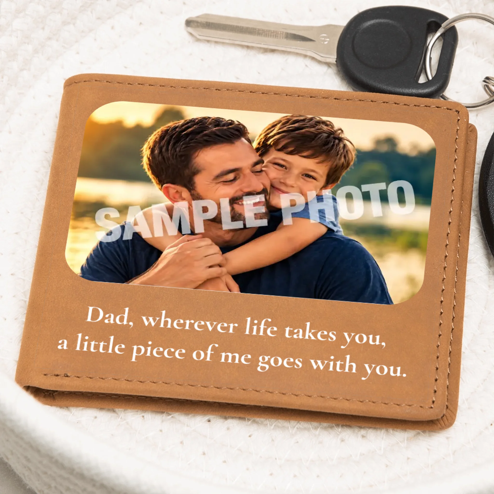 A tan leather wallet or keepsake card shown on a white textured surface with a key partly visible at the top. The wallet has a photo window displaying a man and child, overlaid with the words “SAMPLE PHOTO,” and printed text below reading, “Dad, wherever life takes you, a little piece of me goes with you.