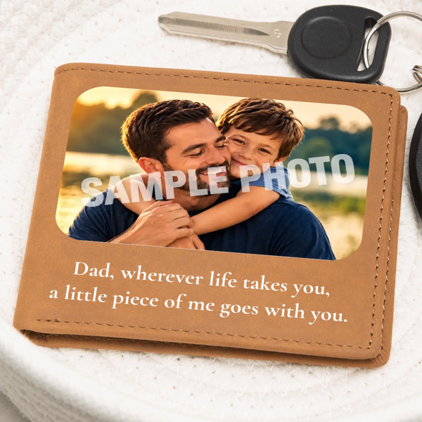A tan leather wallet or keepsake card shown on a white textured surface with a key partly visible at the top. The wallet has a photo window displaying a man and child, overlaid with the words “SAMPLE PHOTO,” and printed text below reading, “Dad, wherever life takes you, a little piece of me goes with you.