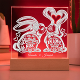 A personalized acrylic LED night light on a wooden base, glowing with a warm red light. The clear panel features white laser-cut butterfly and heart designs with the text 'I STILL GET Butterflies WITH EVERY KISS.