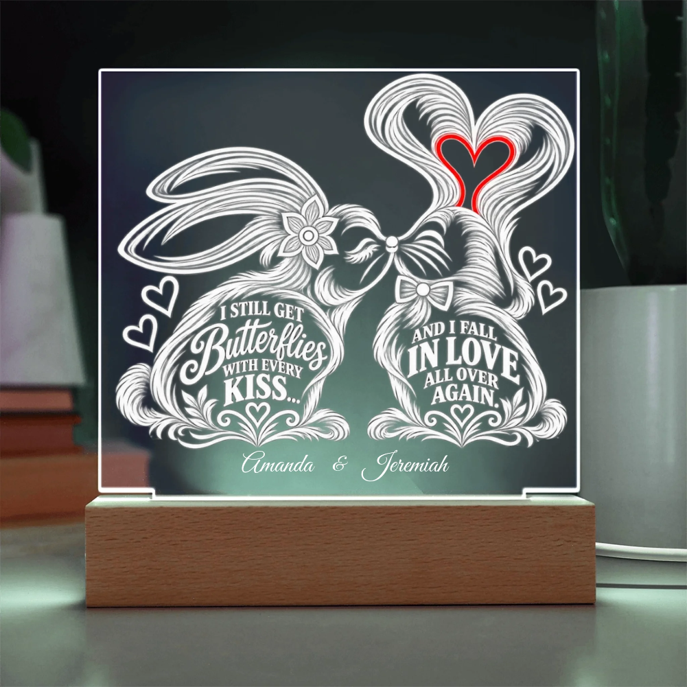 A personalized acrylic LED light sign on a wooden base, featuring two rabbits kissing with decorative white line art and text that reads 'I STILL GET Butterflies WITH EVERY KISS.