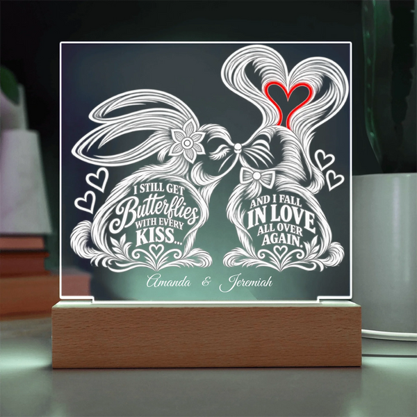 A personalized acrylic LED light sign on a wooden base, featuring two rabbits kissing with decorative white line art and text that reads 'I STILL GET Butterflies WITH EVERY KISS.