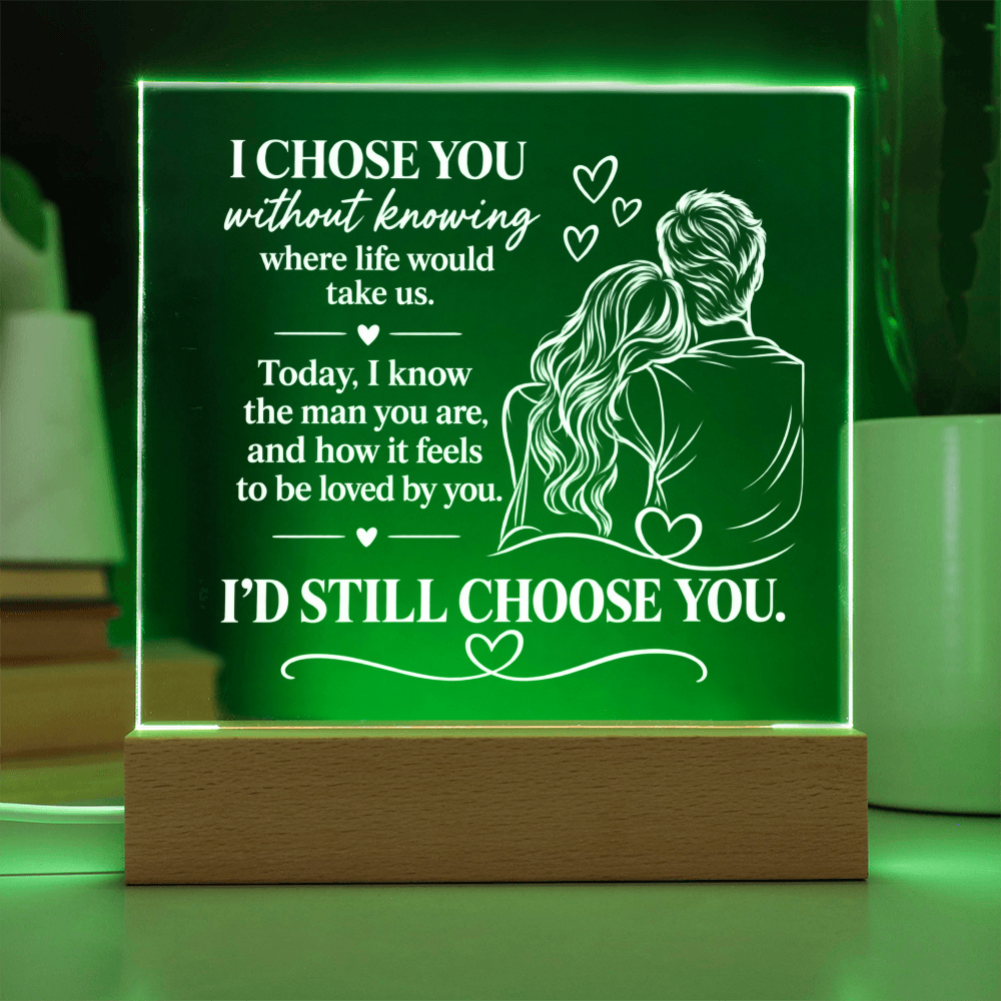 A rectangular LED light box with a wooden base glowing green, featuring white engraved text and an illustration of a couple, set against a softly blurred background.