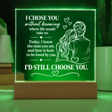 A rectangular LED light box with a wooden base glowing green, featuring white engraved text and an illustration of a couple, set against a softly blurred background.
