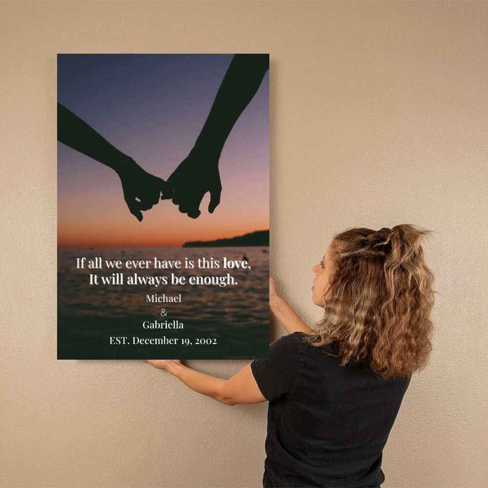 Person hanging a wall art print with hands holding hands over water and sunset text.