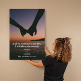 Person hanging a wall art print with hands holding hands over water and sunset text.