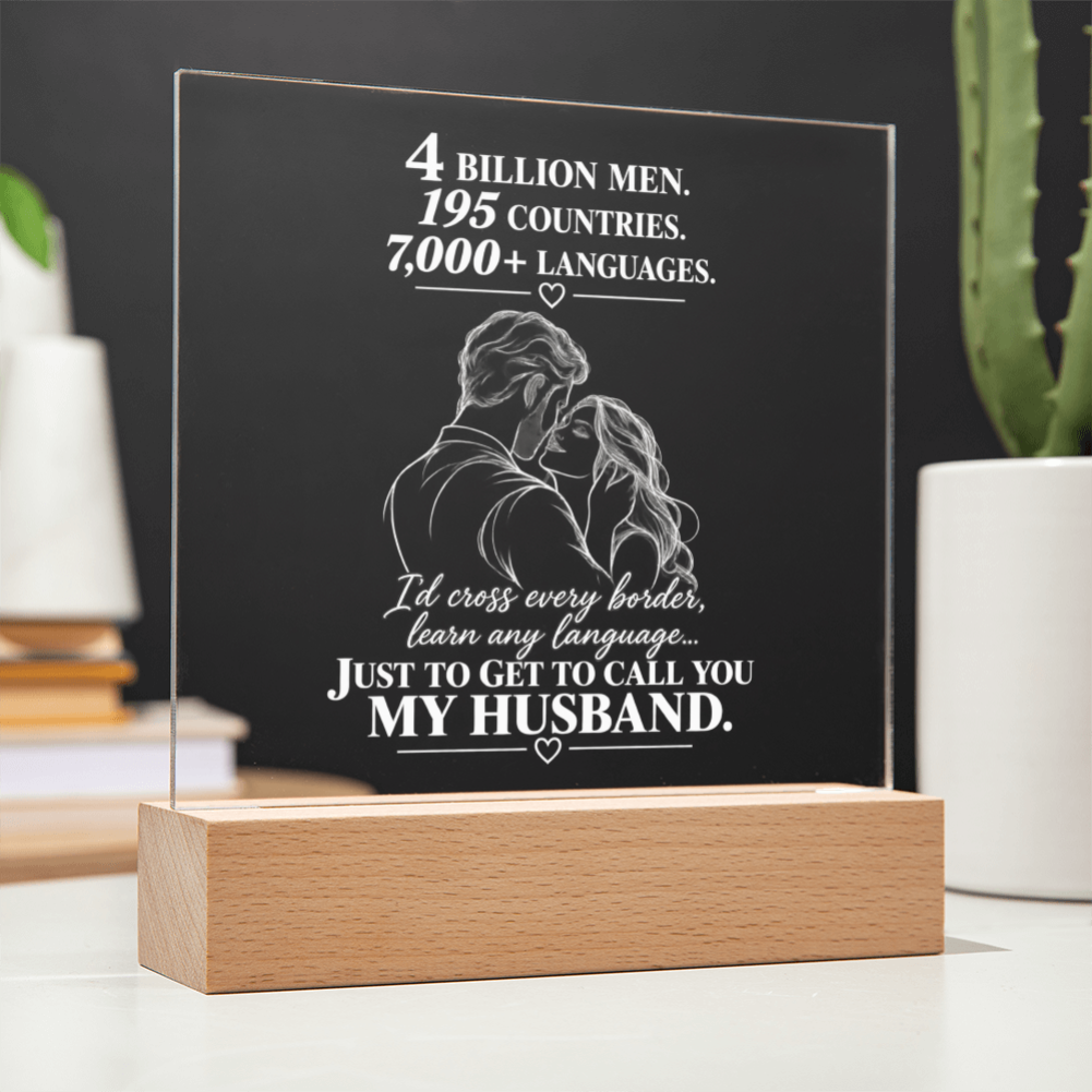 A personalized acrylic LED light plaque on a wooden base, featuring a white engraved illustration of a couple and a touching quote about love, displayed on a tabletop with blurred plants and books in the background.