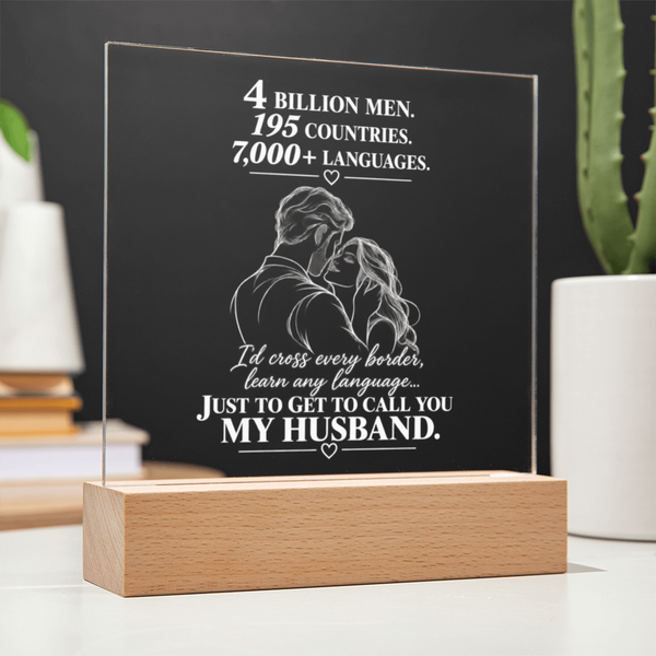 A personalized acrylic LED light plaque on a wooden base, featuring a white engraved illustration of a couple and a touching quote about love, displayed on a tabletop with blurred plants and books in the background.
