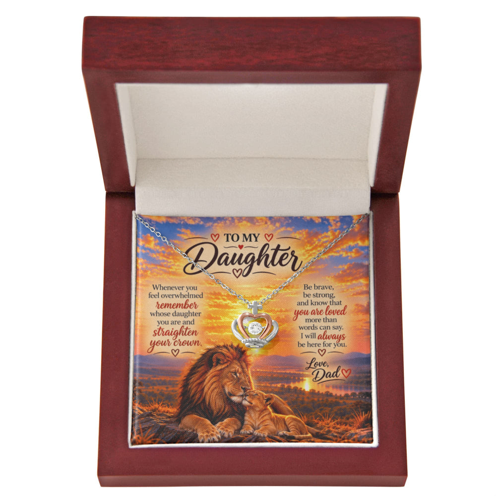 A personalized necklace presented inside an open reddish-brown wooden gift box. The necklace has a silver-toned pendant with a heart-shaped cutout showing a lion cub illustration, and it is displayed over a printed card that reads 'TO MY Daughter' with a sunset background and a lion scene.