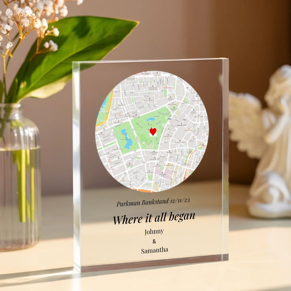 Personalized map in a glass frame on a decorative surface with flowers and a statue.