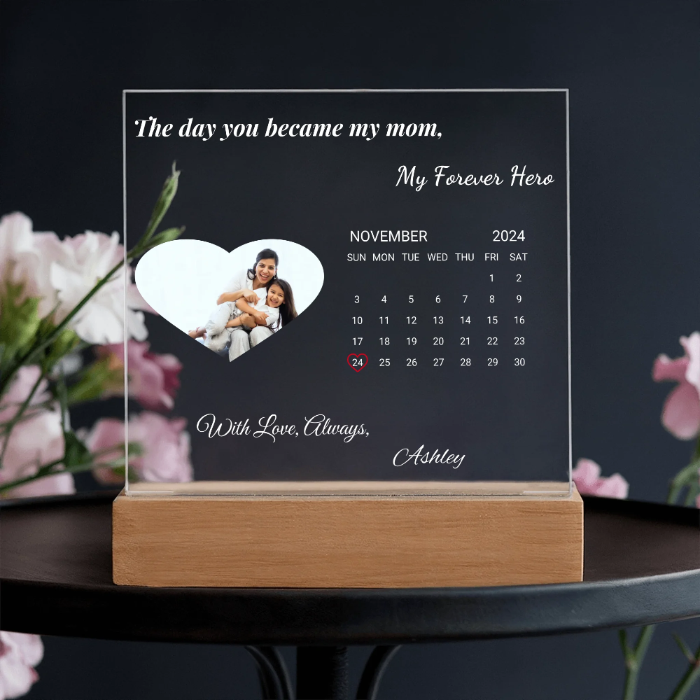 Personalized calendar with a heart-shaped photo of a family on a wooden stand, against a dark background with flowers.