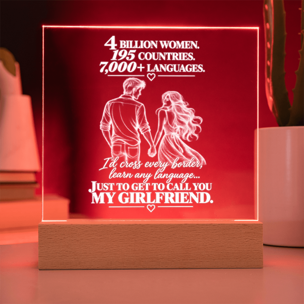 A square acrylic LED lamp on a wooden base, glowing red with white text and an illustration of a couple holding hands. The text reads, '4 BILLION WOMEN, 195 COUNTRIES, 7,000+ LANGUAGES.