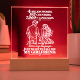 A square acrylic LED lamp on a wooden base, glowing red with white text and an illustration of a couple holding hands. The text reads, '4 BILLION WOMEN, 195 COUNTRIES, 7,000+ LANGUAGES.